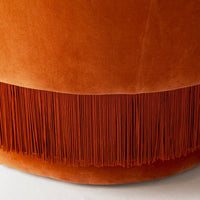 Orange velvet pouf with a fringe pattern in a vibrant, rust shade, enhancing modern décor aesthetics.