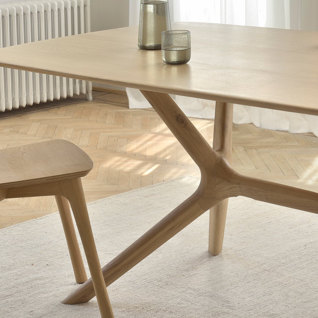 Light natural wood table with a minimalist design and sleek, angular legs, complementing a soft, neutral rug.