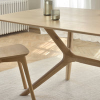 Light natural wood table with a minimalist design and sleek, angular legs, complementing a soft, neutral rug.