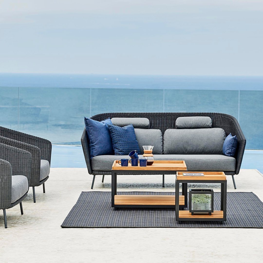 Gray and blue outdoor sofa set with wooden accents, featuring a textured black rug and coastal view backdrop.