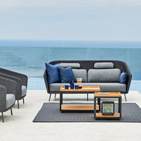 Gray and blue outdoor sofa set with wooden accents, featuring a textured black rug and coastal view backdrop.
