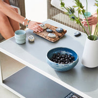 Blue ceramic bowl with black olives, gray table, textured stoneware, and light blue cups on a modern patio setting.