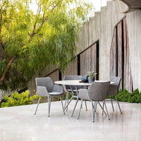 Gray woven pattern dining chairs with sleek silver legs around a light gray table in a modern outdoor setting.