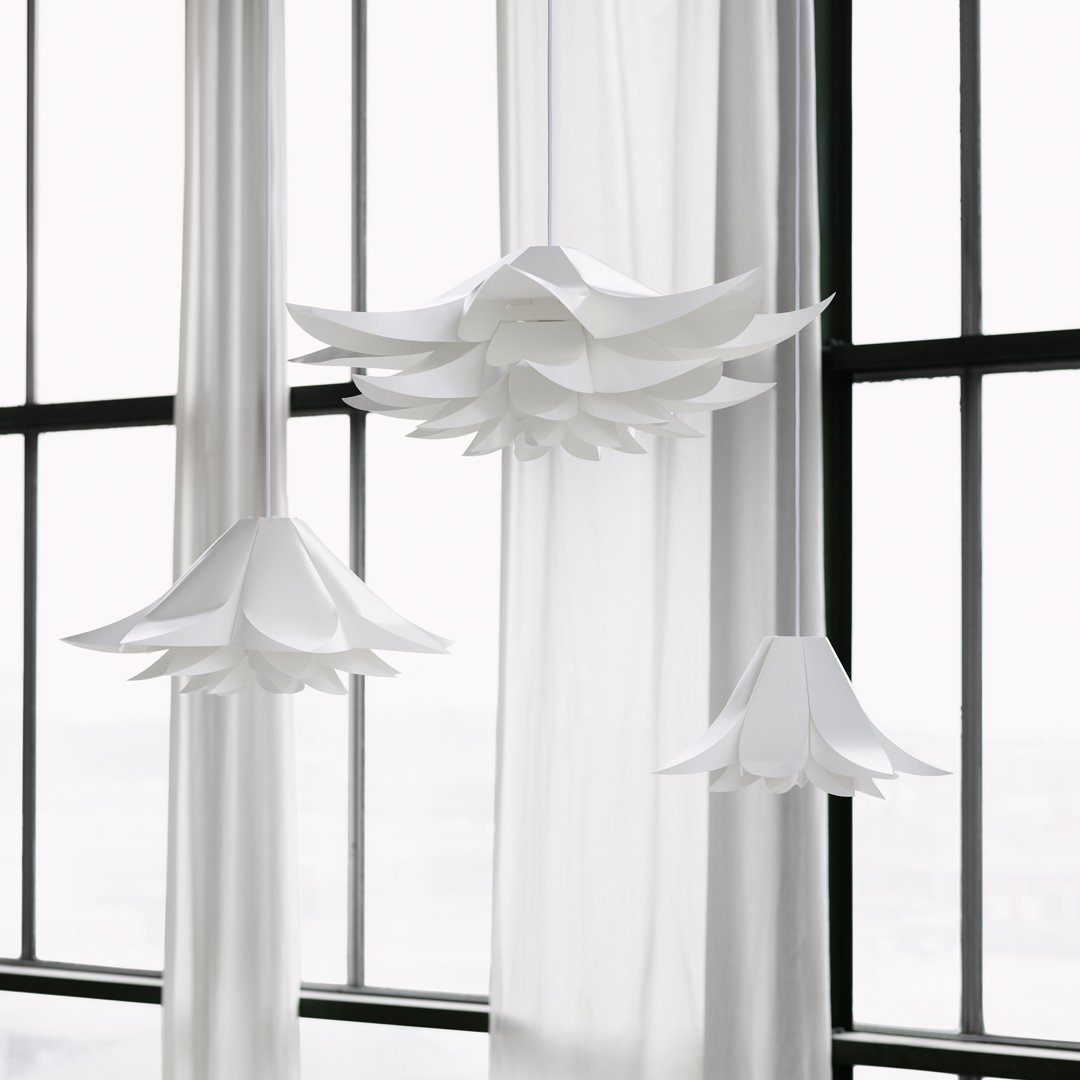 White flower-shaped pendant lights with layered petals, hanging against sheer white curtains.