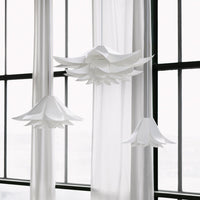 White flower-shaped pendant lights with layered petals, hanging against sheer white curtains.