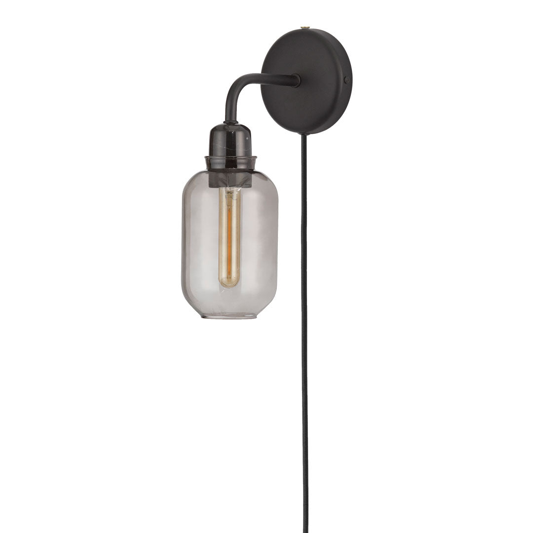 Black wall sconce with clear glass shade and warm-toned filament bulb, featuring a sleek, modern design.