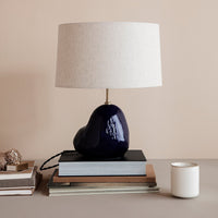 Navy blue ceramic lamp with a textured white shade, placed on stacked books against a soft beige background.