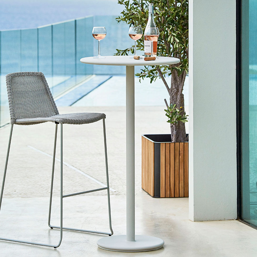 Gray bar stool and white round table against a backdrop of glass and wood, with a scenic outdoor view.