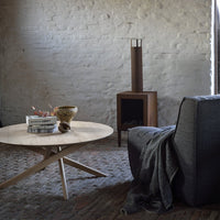 Round wooden coffee table with light finish, dark gray sofa with textured pattern, and neutral-toned woven rug.