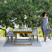 Gray outdoor dining set with a wooden table, light gray cushioned chairs, and a textured rug on a natural wood patio.
