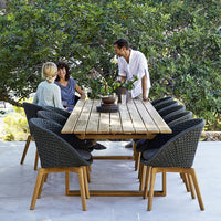"Elegant wooden dining table with woven black chairs, surrounded by lush greenery."