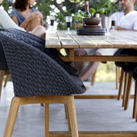 "Elegant black woven chair with wooden legs, paired with a natural wood dining table in a stylish outdoor setting."