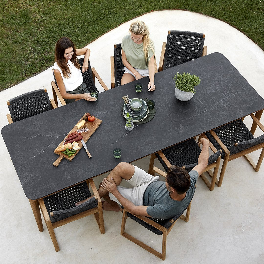 Elegant black stone dining table with natural wood accents, surrounded by stylish black and beige patio chairs.