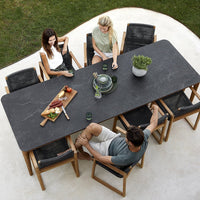 Elegant black stone dining table with natural wood accents, surrounded by stylish black and beige patio chairs.