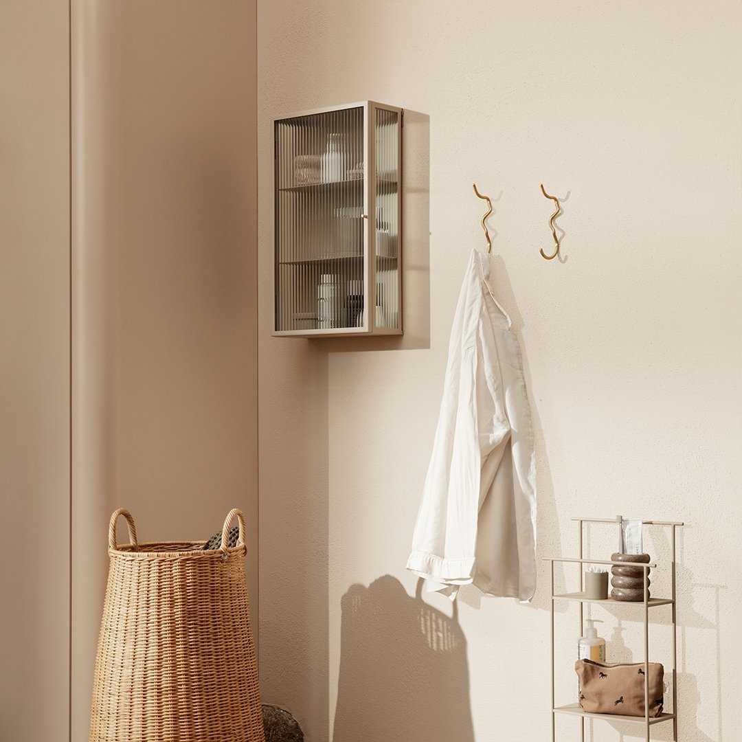 "Minimalist glass cabinet with a silver frame, soft beige wall, and natural woven basket in neutral tones."