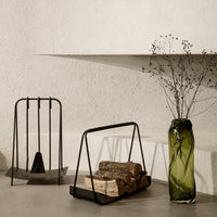 Black metal fireplace tools and holder with a textured green glass vase, showcasing earthy tones and modern shapes.