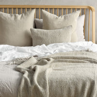 Neutral beige bedding with textured throw and soft white accents, featuring various cushion sizes and patterns.
