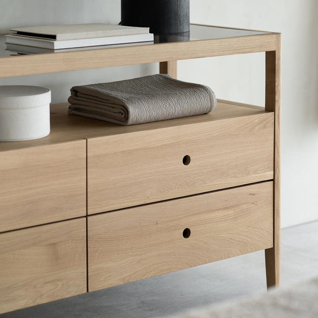 Light oak wood console table with textured gray towels and modern minimalist design. Glass top adds elegant contrast.