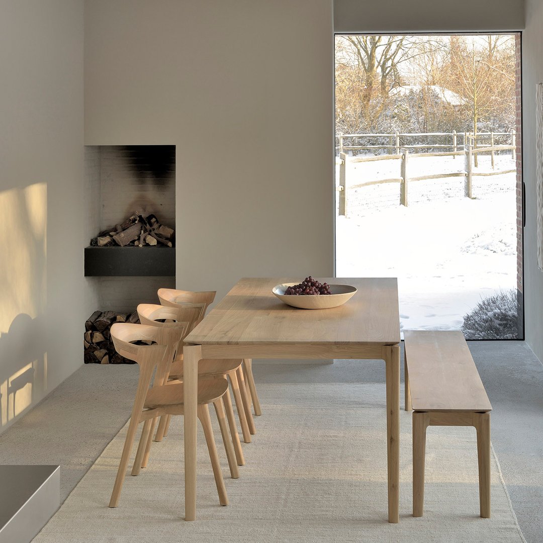 Light wooden dining table with matching chairs and bench, complemented by neutral gray walls and a soft winter light ambiance.