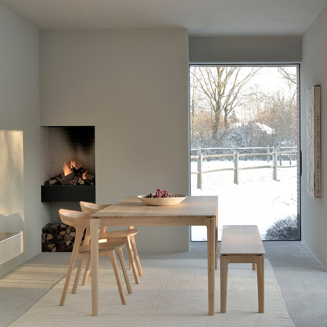 Light grey walls and furniture with natural wood tones create a cozy, minimalist dining space with a subtle winter view.