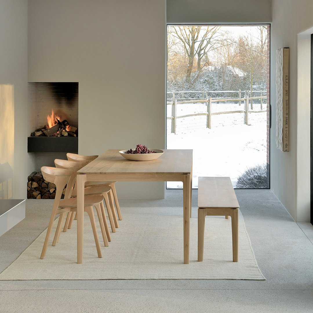 Light wooden dining table with natural finish, paired with matching chairs and a simple, neutral rug in a cozy, modern setting.