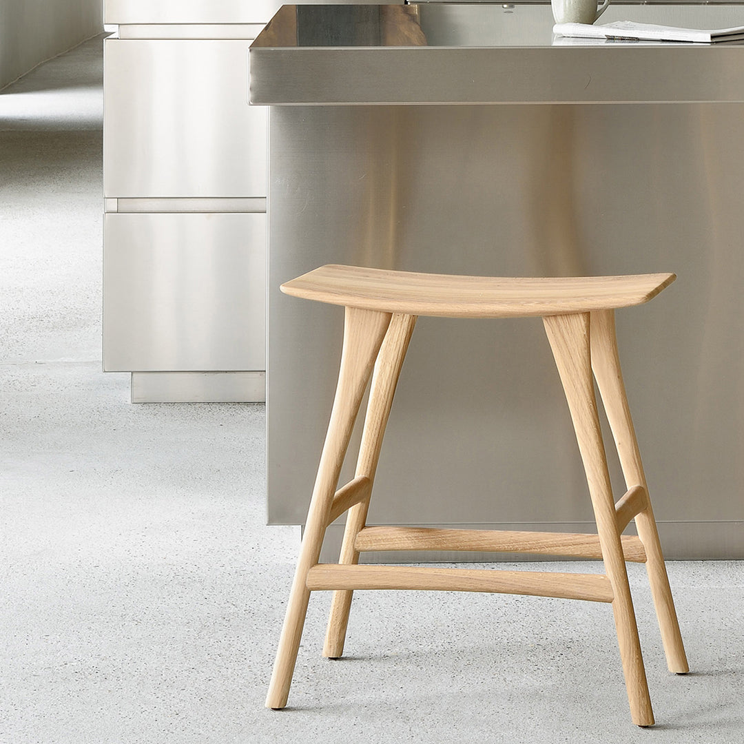 Light natural wood stool with a smooth, curved seat and minimalist design, set against a neutral-toned kitchen backdrop.