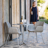 Gray woven chairs with a modern geometric pattern, paired with a sleek round table, set against a rustic background.