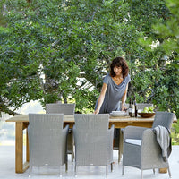 "Elegant gray wicker dining set with natural wood table, perfect for outdoor entertaining in a lush green setting."