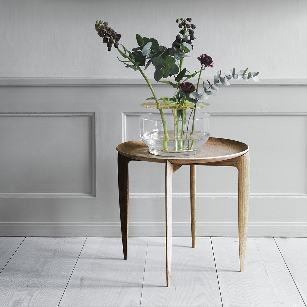 Round wooden side table with a warm beige tone and sleek, minimal design, featuring a smooth surface and tapered legs.