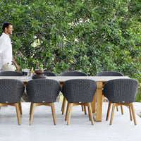 Outdoor dining set featuring charcoal woven chairs and a natural wood table against lush green foliage.