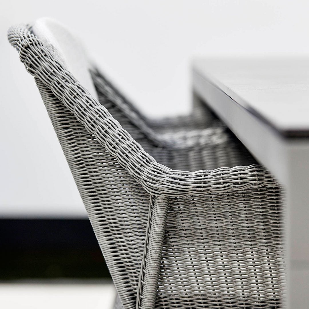 Gray woven patio chair with a sleek design, featuring intricate basketweave patterns and white cushion accents.