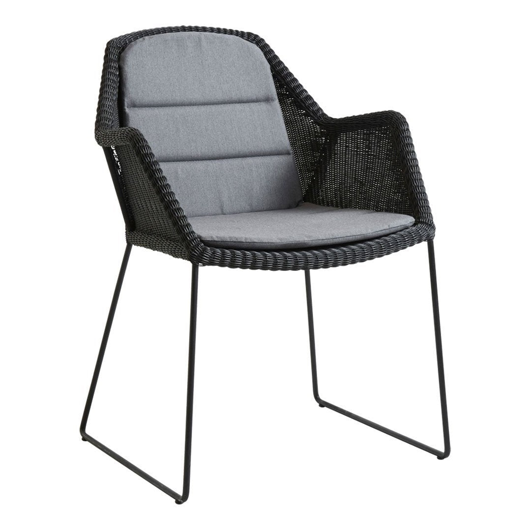Gray cushioned chair with a woven black rattan frame and sleek metal legs, featuring a modern, minimalistic design.
