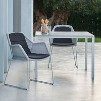 Gray wicker chairs with black cushions beside a sleek, white table on a concrete surface.