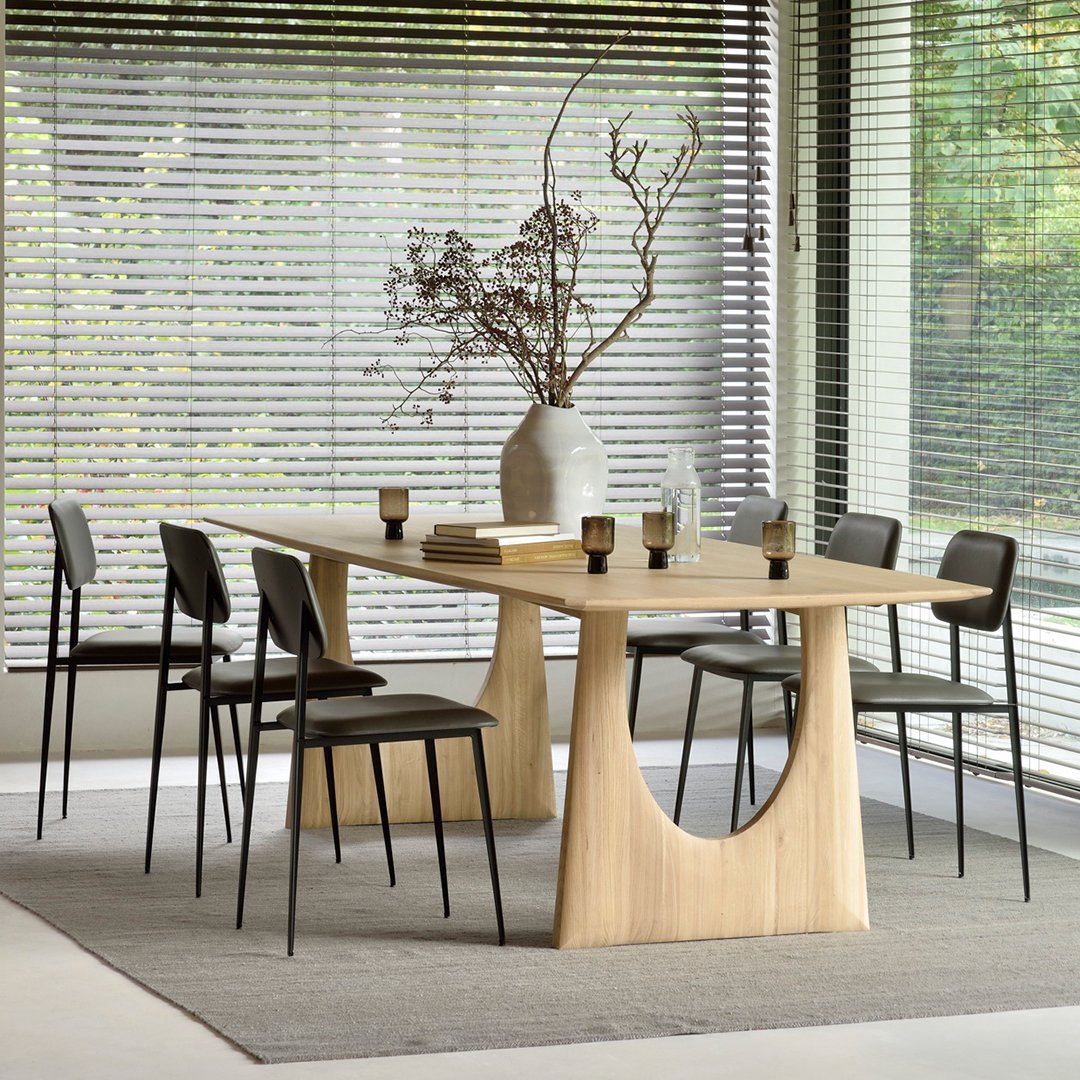 Natural wood dining table with a light finish, paired with sleek black chairs on a neutral-toned rug.