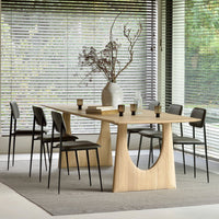 Natural wood dining table with a light finish, paired with sleek black chairs on a neutral-toned rug.