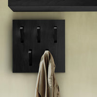 Black wall-mounted coat rack with sleek, matte hooks against a light beige wall for a modern, minimalist look.