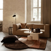 Beige sofa with brown and rust accent pillows, geometric patterned rug in earthy tones of brown, terracotta, and cream.