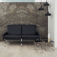 Modern black sofa against a textured gray wall with gold accents, complemented by clear glass side tables.