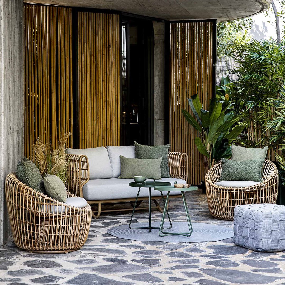 Stylish outdoor seating set with light gray cushions, green accents, and natural woven patterns on rattan furniture.