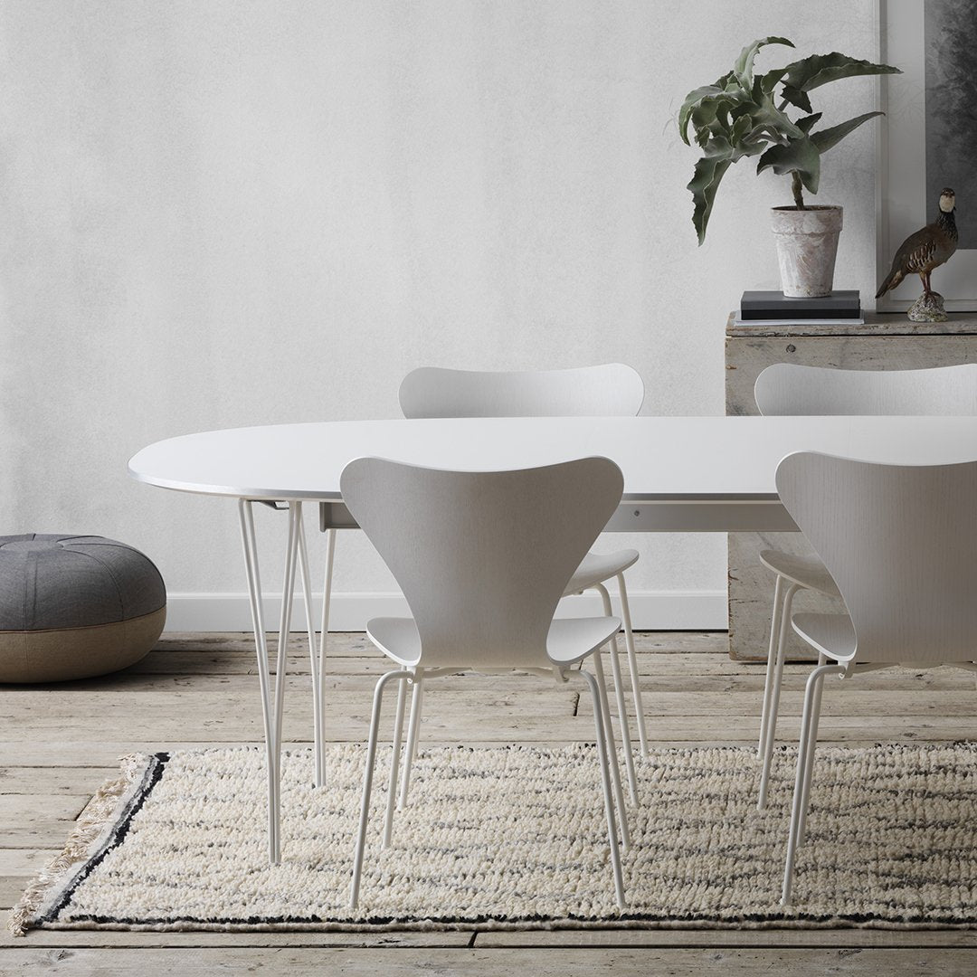 White oval dining table with minimalist design, surrounded by sleek white chairs on a textured beige area rug.
