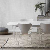 White oval dining table with minimalist design, surrounded by sleek white chairs on a textured beige area rug.