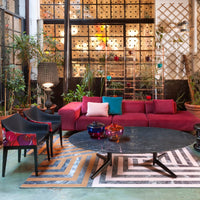 Vibrant pink sofa, patterned chairs, black round table, colorful decor, and geometric rug in a stylish living space.