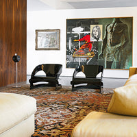 "Contemporary living room featuring black chairs, vibrant abstract art, and a warm-patterned area rug in earthy tones."