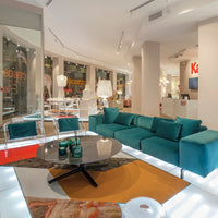 Teal sectional sofa, geometric area rug with orange and cream accents, modern glass coffee table, and bright open space.