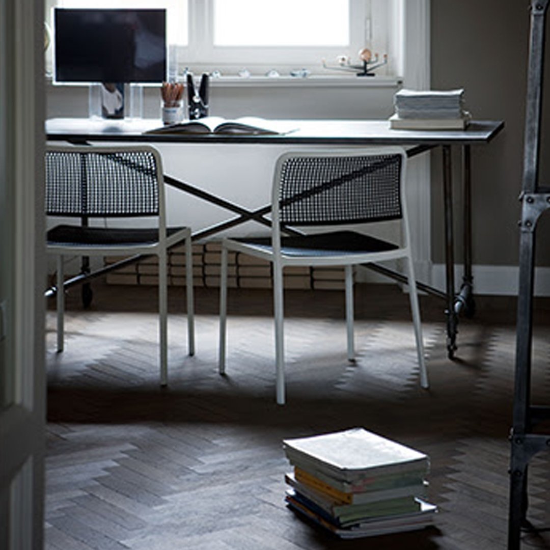 Modern black and white desk with mesh chairs on herringbone wood floor, accentuated by soft gray walls.