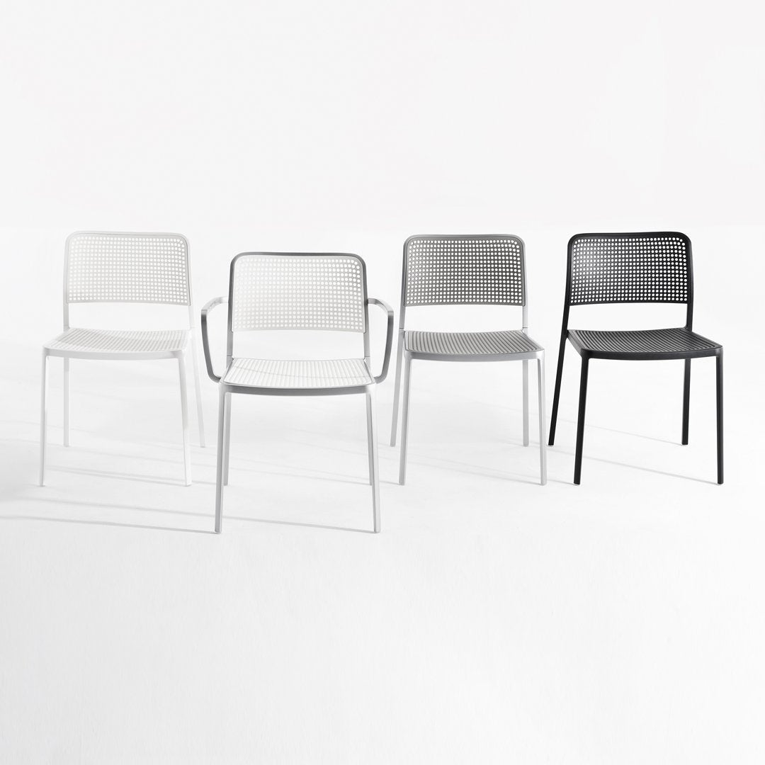 "Set of four modern chairs in white, light gray, dark gray, and black with a sleek, perforated design."