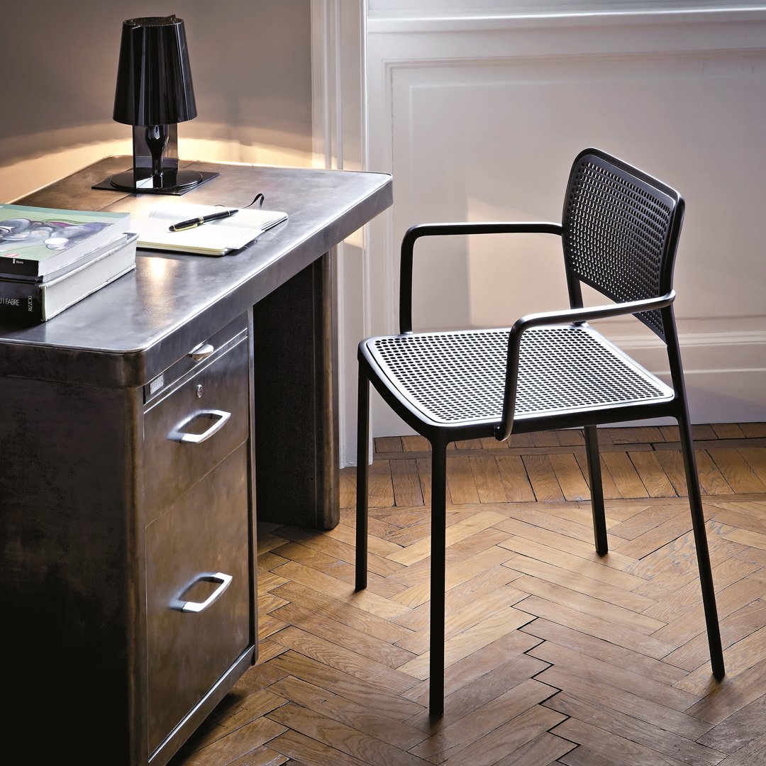 Black mesh chair with a sleek design, featuring geometric patterns, set against a warm wooden floor and metallic desk.
