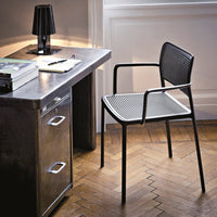 Black mesh chair with a sleek design, featuring geometric patterns, set against a warm wooden floor and metallic desk.