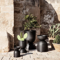 Black ceramic planters in varying heights and shapes, showcasing minimalistic design against a rustic stone backdrop.