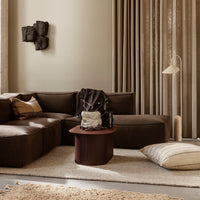 Stylish brown couch with beige accents, textured throw pillows, and a circular maroon coffee table in a warm-toned living space.